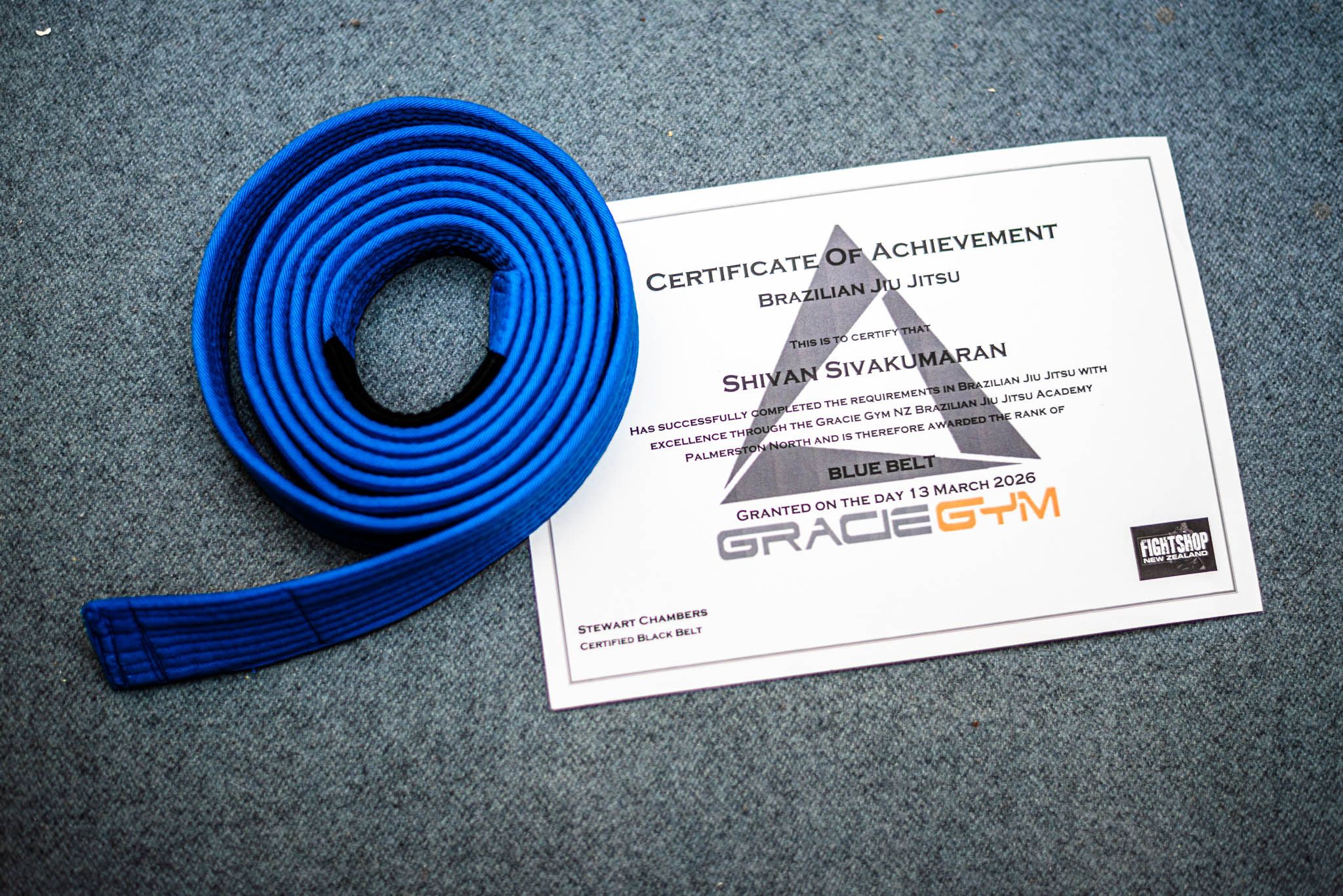 A coiled BJJ Blue belt on top of a certificate