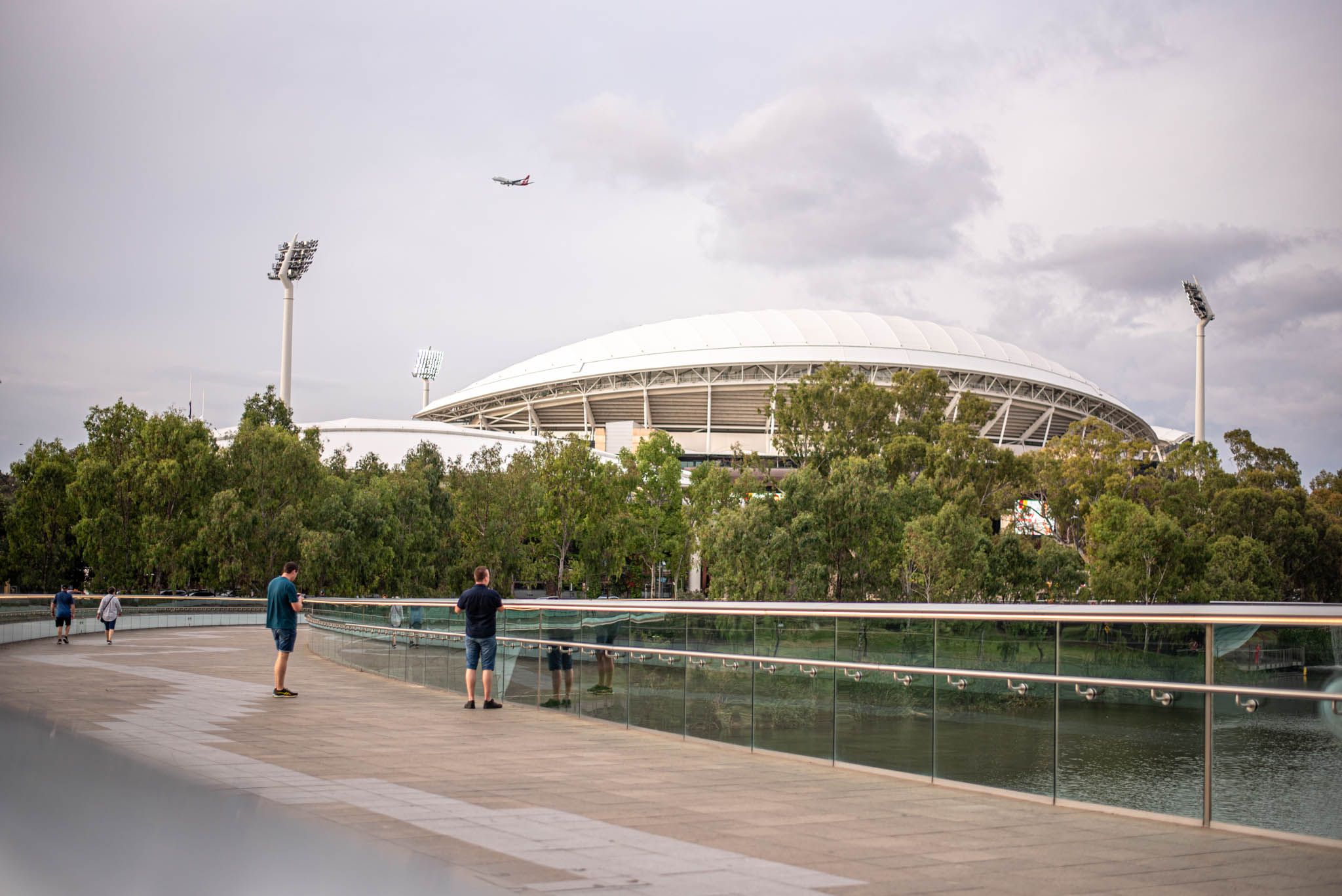 A stadium in the distance with a plane flying overhead. The stadium is the Adelaide Oval