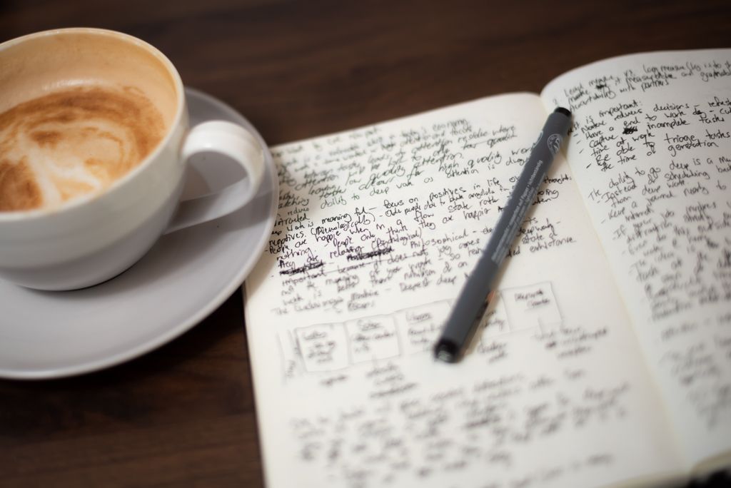 A coffee, book with black handwriting and a pen on top